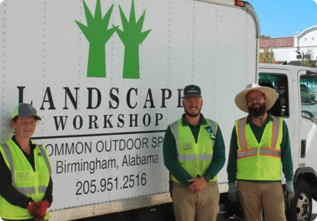 Three workers stand smiling in front of a white Landscape Workshop truck.