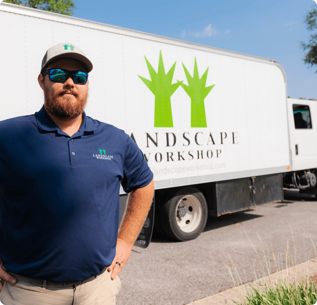 Man stands in front of white Landscape Workshop landscaping truck on a sunny day.