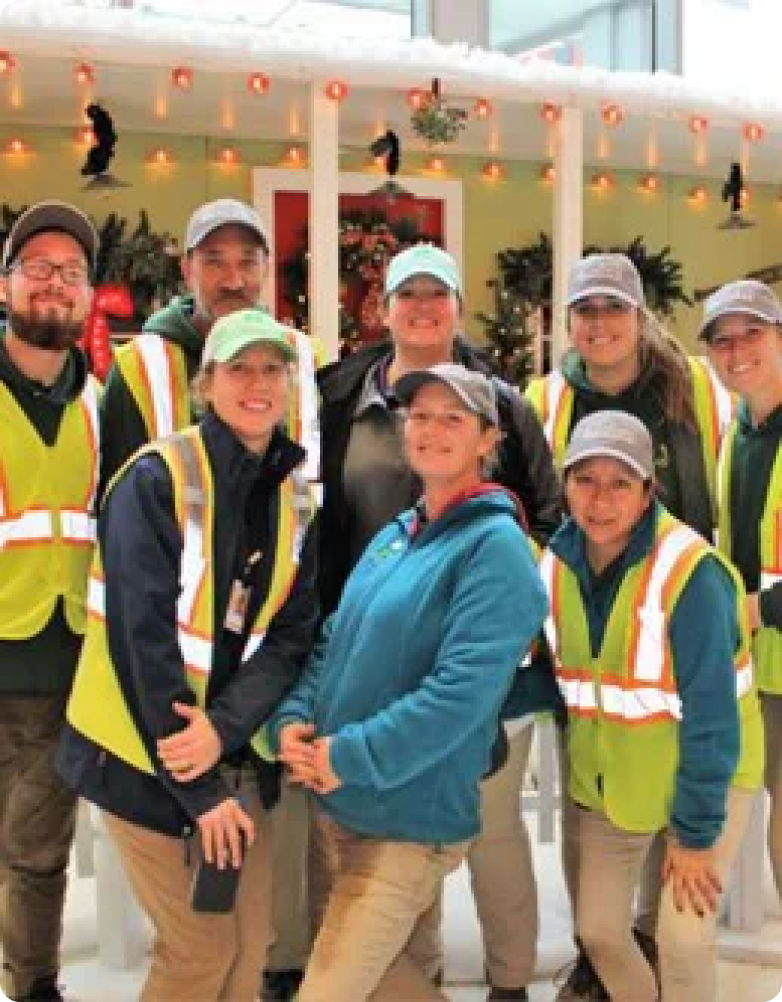 Seven people in work attire posing happily with a snow-covered gazebo and holiday decorations in the background.