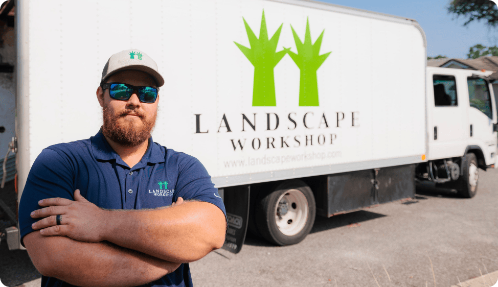 Man stands in front of white Landscape Workshop landscaping truck on a sunny day.